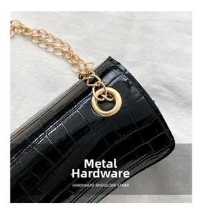 Detail of black croc-embossed leather texture with golden eyelet and chain shoulder strap