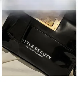 Close-up of black patent leather phone bag with golden twist lock and white typography