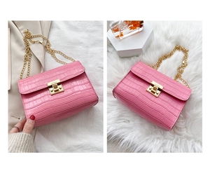 Detail of pink crocodile embossed leather bag with golden metal rotary lock and chain