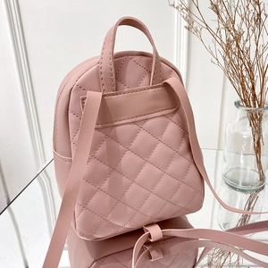 Mini pink quilted backpack with rhombus pattern and slim straps on a glass display
