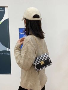 Detail of houndstooth crossbody bag featuring golden metal clasp and chain strap