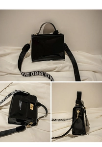Detail of black patent leather bag featuring gold twist lock and chic lettered strap
