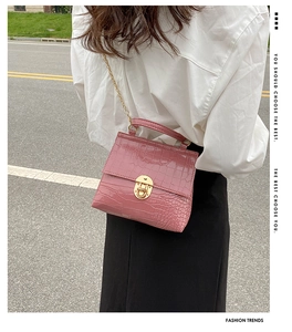 Pink croc-embossed mini handbag featuring a gold twist lock and metal chain strap on model