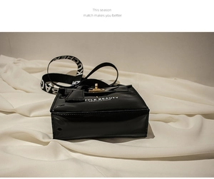 Detail of black glossy patent leather mini bag with gold buckle and wide letter strap