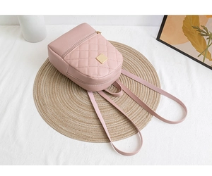 Detailed view of pink quilted small backpack with gold hardware on a straw mat