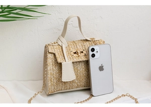 Detail view of straw woven crossbody bag with gold lock next to a smartphone for size reference