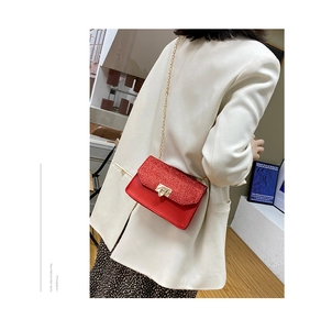 Détail du sac bandoulière à paillettes rouges avec chaîne dorée sur blazer blanc