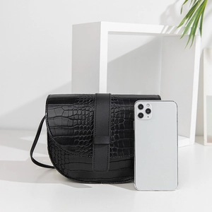 Borsa a tracolla nera a sella con trama coccodrillo e smartphone per scala dimensionale