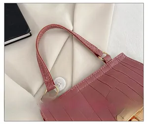 Close-up of pink croc-embossed mini handbag featuring gold metal buckles and top handle
