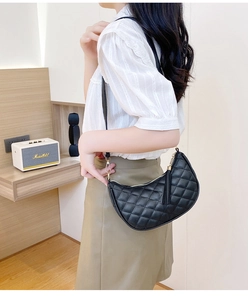 Detail shot of a black quilted crescent bag featuring a tassel and gold hardware