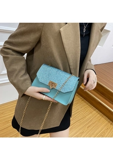 Détail du sac à bandoulière bleu clair à paillettes avec chaîne dorée sur blazer brun