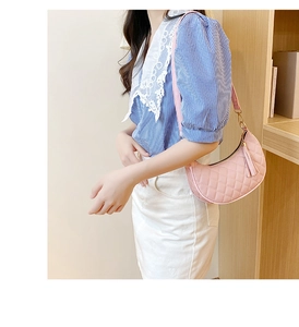 Sac bandoulière demi-lune rose matelassé avec pompon et détails dorés porté par mannequin