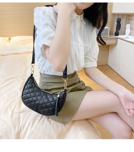 Détail du sac demi-lune noir matelassé avec fermeture dorée et pompon en cuir élégant