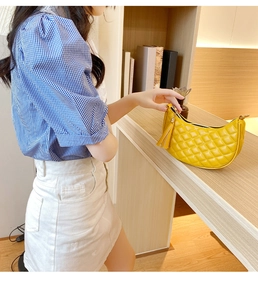 Détail d'un sac demi-lune matelassé jaune avec pompon et fermeture éclair dorée