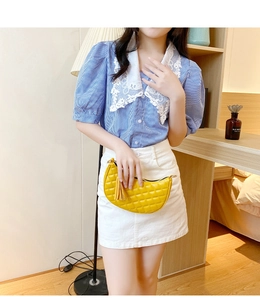 Close-up of a yellow quilted crescent handbag with decorative tassel on model outfit