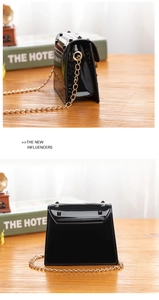 Detail of black glossy jelly bag with gold studs and delicate chain strap on desk