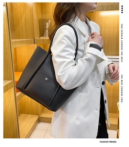 Detail view of large black minimalist tote bag with silver side button on model