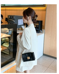 Détail du sac à bandoulière noir matelassé avec chaîne dorée dans un décor de café
