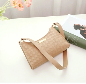 Detail of beige shoulder bag with checkered texture and gold metal plaque on white table