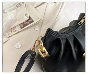 Detail shot of black ruched leather handbag with a chunky gold chain and pleated texture
