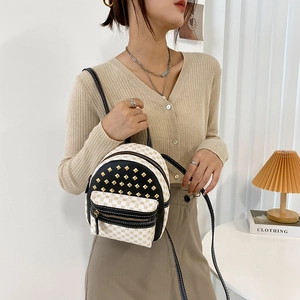 Mini backpack with beige print and gold studs, worn by model in a stylish indoor setting