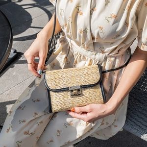 Ladies straw woven crossbody bag with black trim and gold square buckle in sunlight
