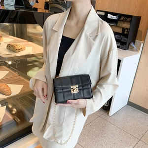 Sac bandoulière matelassé noir avec chaîne dorée et fermoir pivotant porté par un mannequin