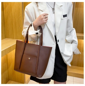 Detail of a large brown leather tote bag with metal snap pocket shown on a model