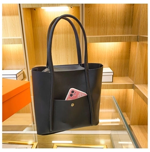 Detail of black matte tote bag featuring an outer pocket with a gold magnetic button