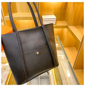 Close-up of black tote bag showing textured faux leather and gold metal button closure