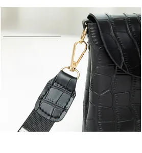 Detail of gold-tone detachable metal clasp on a black crocodile pattern crossbody bag