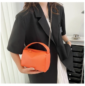 Detail of orange lychee grain leather pillow bag with gold chain and ring zipper pull