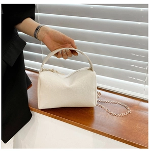 Close-up of white lychee textured women handbag with golden chain and curved handle