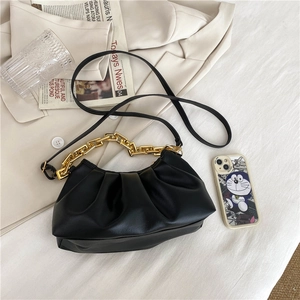 Chic black pleated cloud bag with gold chain strap styled on an ivory blazer backdrop