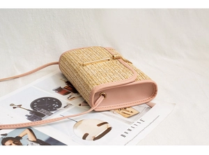 Detail of woven straw crossbody bag with pink faux leather trim and gold T-bar buckle