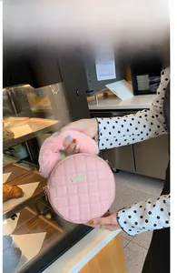 Détail d'un sac rond rose matelassé avec poignée en peluche et plaque en métal devant