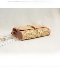 Detail of woven straw crossbody bag with pink faux leather trim and gold tassel charm