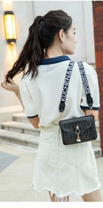 Detail of black crocodile texture mini bag with pearl charm and wide letter strap
