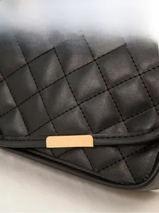 Detailed macro view of black quilted leather texture and premium gold metal hardware on bag