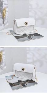 Detailed view of the heart-shaped gold clasp and white quilted texture of the chain bag