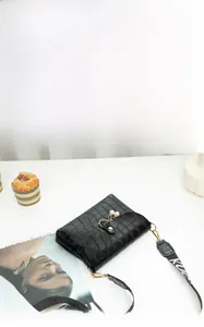 Detail of black crocodile texture mini bag with pearl charm and wide lettered strap