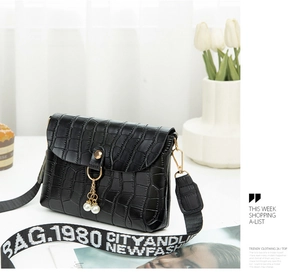Detail of crocodile pattern small square bag featuring pearl pendant and wide lettered strap