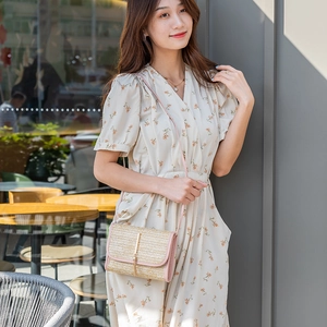 Pink straw crossbody bag with leather trim and gold buckle, worn with a floral dress