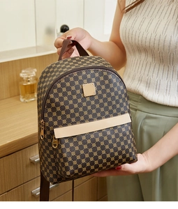 Detail of a brown printed backpack with gold hardware held by a hand in a warm setting