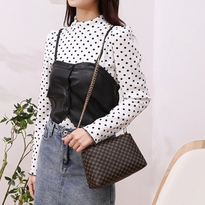 Brown floral crossbody bag with gold chain strap shown on a model in a stylish interior