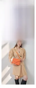 Detail of orange pebble leather crossbody bag with gold lock and chain on fashion model
