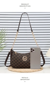 Detail view of crescent shoulder bag with letter print and metal chain strap beside phone