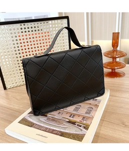 Detailed view of black quilted leather handbag with gold hardware on a white book