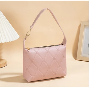 Detail einer hellrosa gesteppten Handtasche mit Goldakzenten und Rautenmuster-Struktur