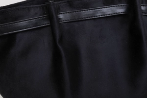 Gros plan du sac cabas en daim noir montrant la bandoulière en cuir et les coutures